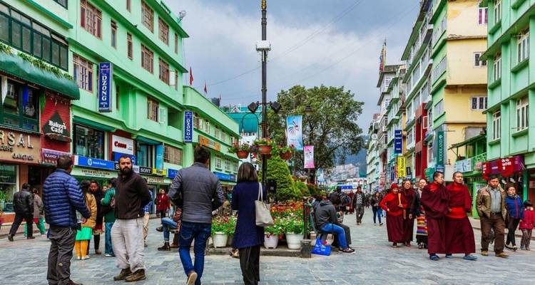 Pedestrian boulevard flanked by pastel green buildings and shops, bustling with locals and monks.