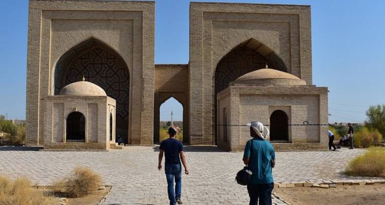 Imagen repetida de visitantes caminando hacia un portal antiguo de doble arco en un paisaje arenoso.
