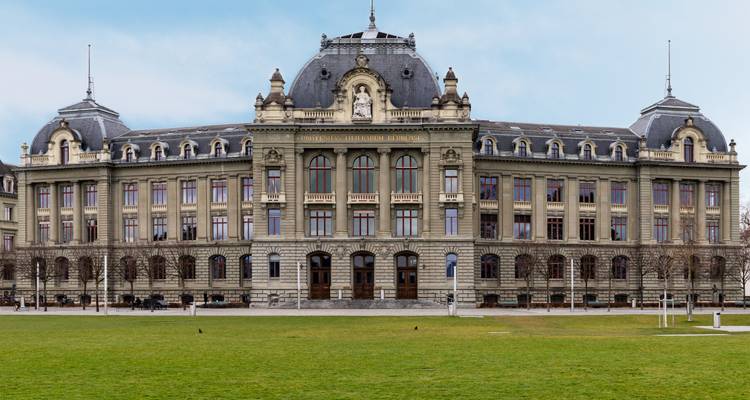 Grand neoclassical Federal Palace building fronting a wide green lawn in Bern under light clouds.