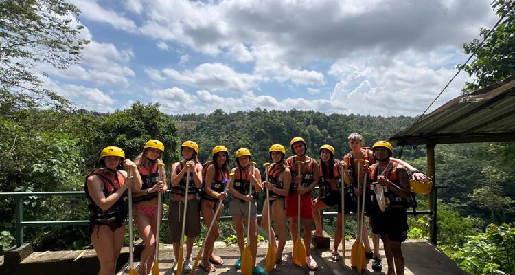 Groupe souriant portant des casques et des gilets de sauvetage pose avec des pagaies avant une aventure de rafting en eaux vives.