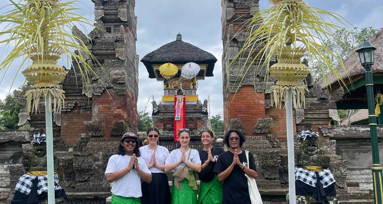 Des voyageurs en sarongs se tiennent les mains jointes en prière devant un portail de temple balinais orné.