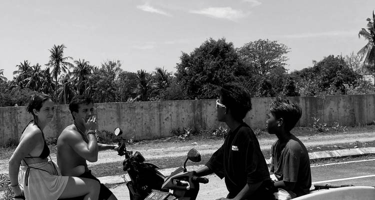 Image en noir et blanc d'amis qui discutent assis sur des motos le long d'une route de campagne.