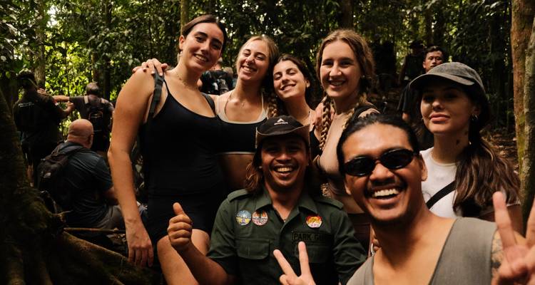 Des randonneurs riant posent avec leur guide parmi d'énormes racines d'arbres dans la forêt tropicale.