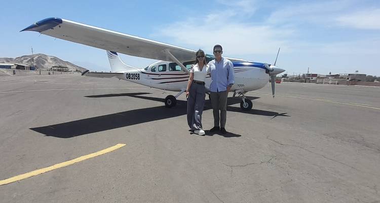 Dos viajeros parados frente a una pequeña aeronave blanca de turismo estacionada en una pista asfaltada bajo el sol abrasador en Nazca.