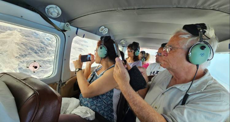 Pasajeros con auriculares fotografían las líneas del desierto de Nazca a través de la ventana de una avioneta.