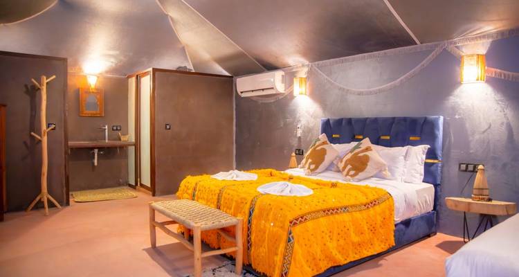 Stylische Wüstencamp-Suite mit Doppelbett, orangefarbenen Decken und sanfter Beleuchtung