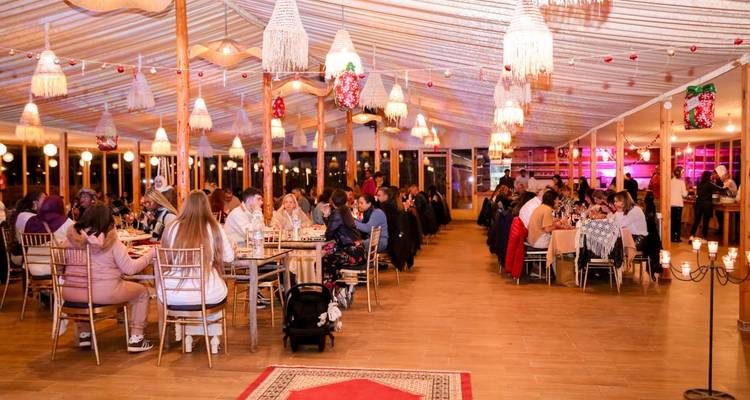 Großes Innenspeisezelt voller Gäste, die unter dekorativen Lichtern eine Mahlzeit genießen