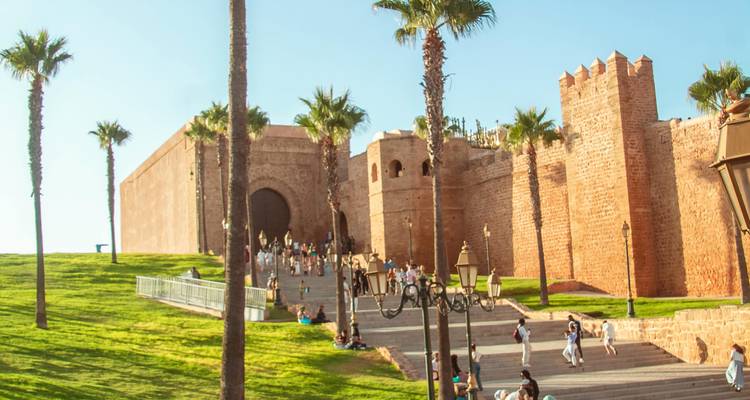 Besucher entspannen auf einem grasbewachsenen Hügel, der zu einem massiven Sandsteintor und den Mauern einer historischen Festung unter warmem Nachmittagslicht führt