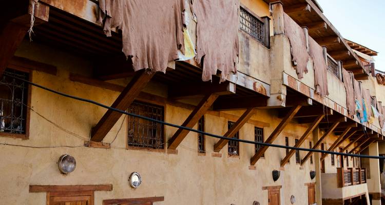 Stapels dierenhuiden hangen over de houten balken van een traditionele leerlooierij in een oud adobe gebouw.