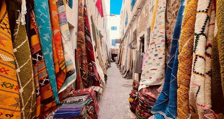 Een smalle steeg behangen met kleurrijke Marokkaanse tapijten en textiel die aan witte muren hangen.