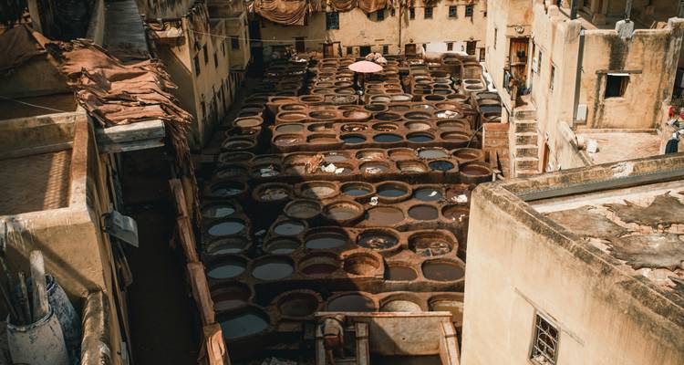 Een verhoogd uitzicht op Fes' ronde verfkuipen met een eenzame arbeider onder een roze parasol.