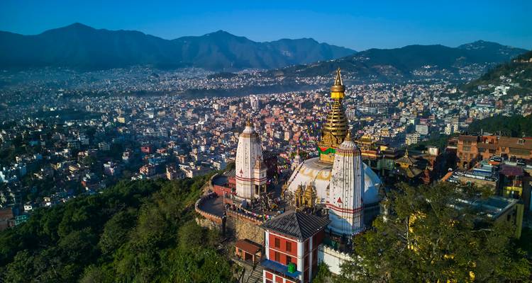 Vue aérienne au lever du soleil du Stupa de Swayambhunath perché sur une colline boisée au-dessus de la vallée tentaculaire de Katmandou et des crêtes montagneuses.