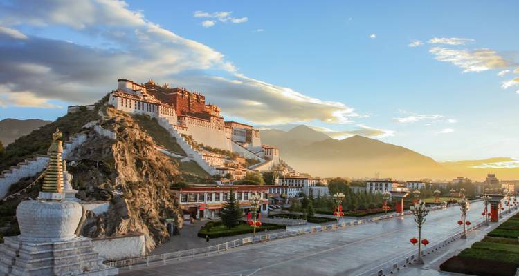 Majestueux Palais du Potala dominant une colline à Lhassa avec des montagnes et une lueur de lever de soleil dans le ciel.