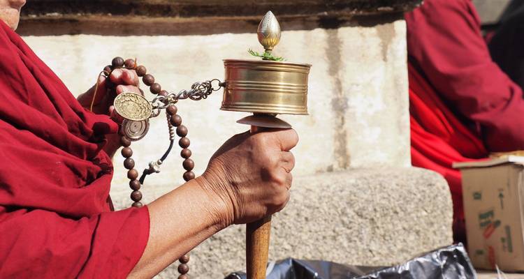 Main de moine tenant un moulin à prières tibétain et un chapelet mala pendant un rituel.