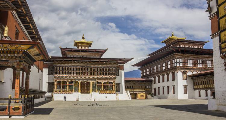 Cour ornée à l'intérieur d'un dzong bhoutanais avec des boiseries complexes, des murs blancs et un visiteur solitaire.