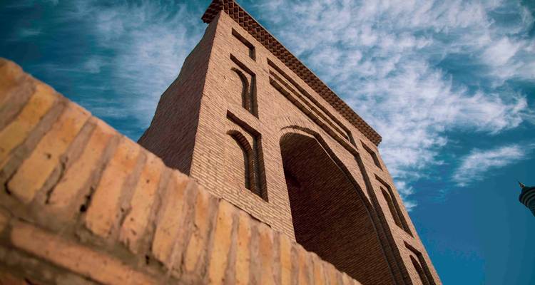 Plan en contre-plongée d'un grand minaret en brique contre un ciel bleu vif strié de nuages effilochés.