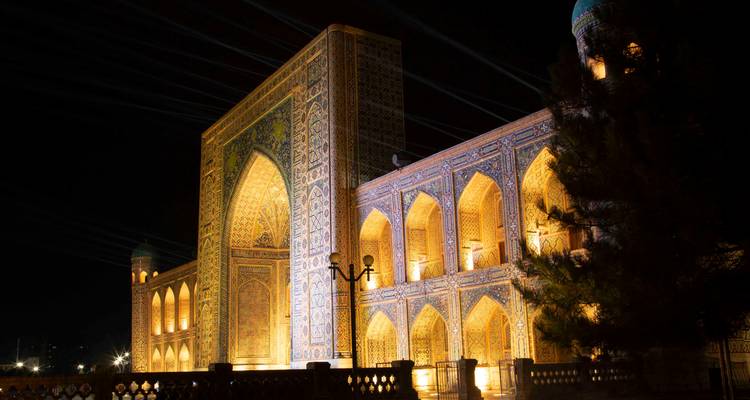Madrasa du Registan illuminée la nuit avec des motifs de mosaïque complexes qui brillent.