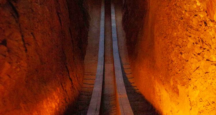 Passage étroit faiblement éclairé ou voies ferrées descendant entre de hauts murs oranges.