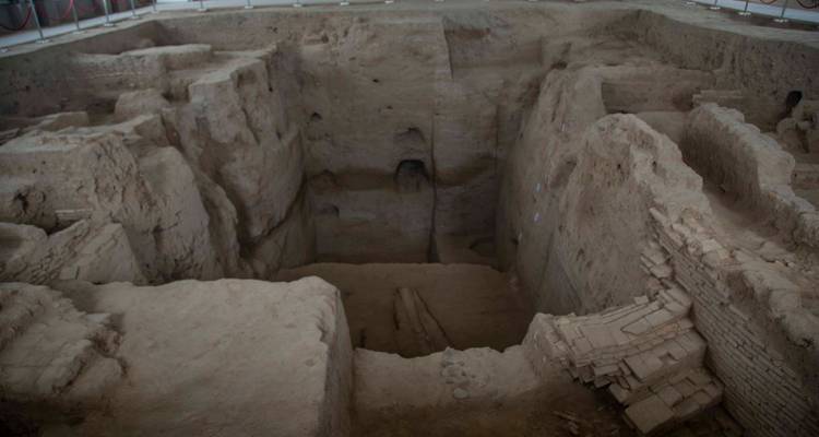 Fosse d'excavation archéologique révélant de profondes couches de briques et de boue d'une structure ancienne.