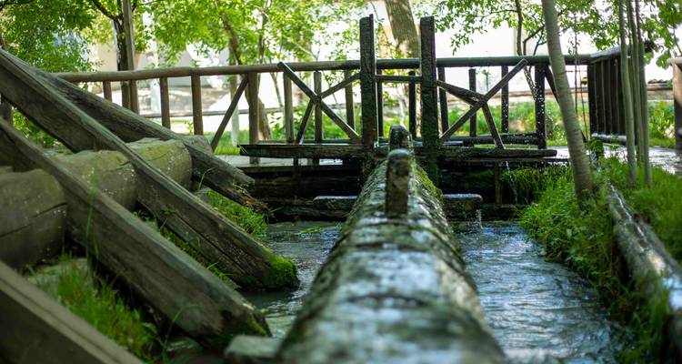 Canal d'eau en bois et écluse dans un jardin ombragé avec ruisseau qui coule.