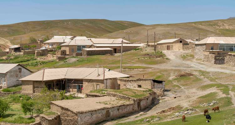 Village de montagne rural avec maisons en pierre, chemins de terre et bétail au pâturage.