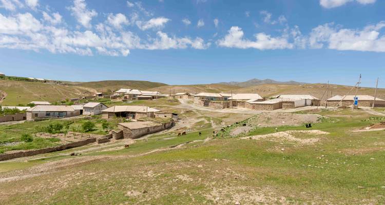 Vaste panorama d'un village ouzbek isolé étalé sur des collines arides vallonnées sous des nuages épars.