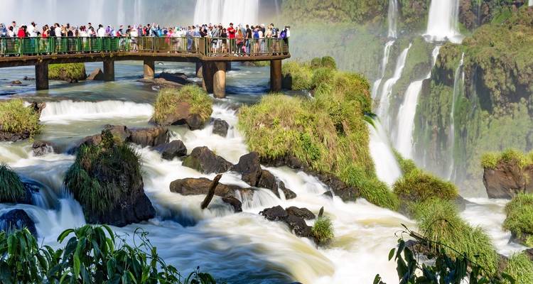 Multitudes en pasarela elevada contemplando las poderosas Cataratas del Iguazú que caen en cascada a través de exuberantes acantilados de la selva.