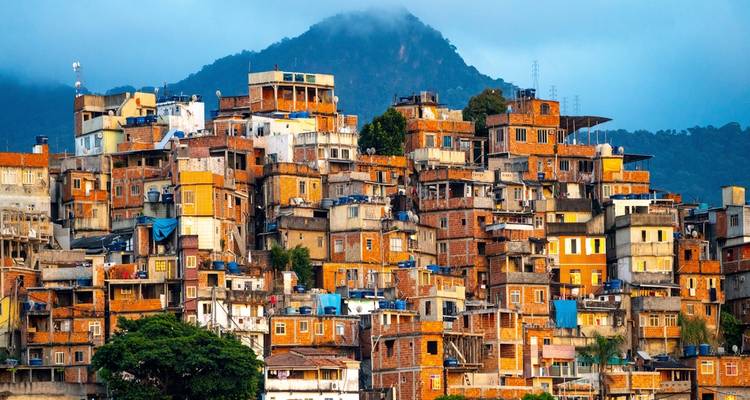 Casas coloridas de favela apiladas subiendo por una ladera bajo un pico montañoso brumoso en Río de Janeiro.