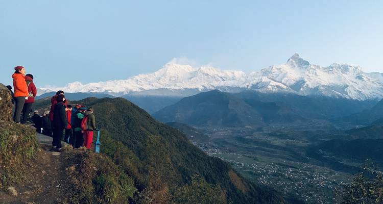 Los viajeros se encuentran en una cresta al amanecer admirando la cordillera Annapurna cubierta de nieve sobre un valle profundo