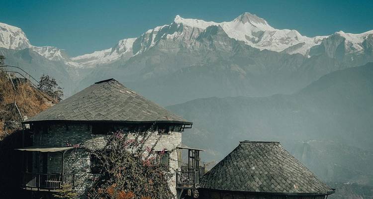Casas de piedra con techos de pizarra se alzan contra un fondo de imponentes picos nevados bajo cielos despejados