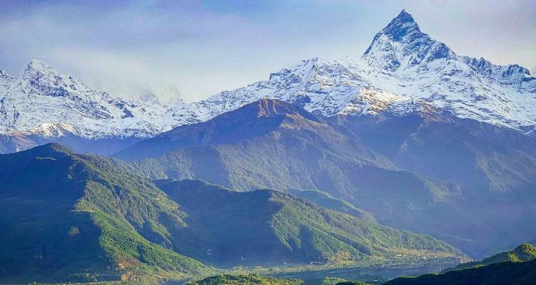 El icónico pico Machapuchare con forma de cola de pez se eleva abruptamente sobre las laderas inferiores boscosas y los pueblos del valle