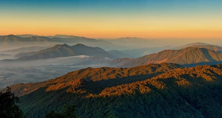 La luz dorada del amanecer pinta las crestas montañosas en capas y los valles brumosos con tonos cálidos