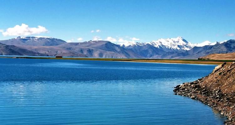 Kristallblauer Hochgebirgssee mit schneebedeckten Himalaya-Gipfeln unter klarem Himmel.