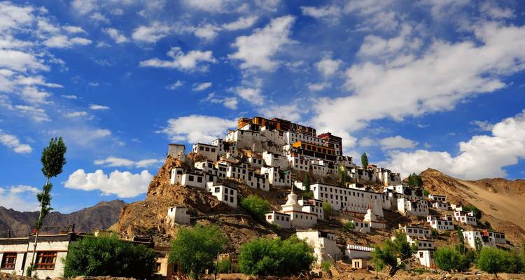 Das weiß getünchte Thiksey-Kloster fällt kaskadenartig einen felsigen Hügel hinab unter einem leuchtend blauen Himmel mit vereinzelten Wolken.