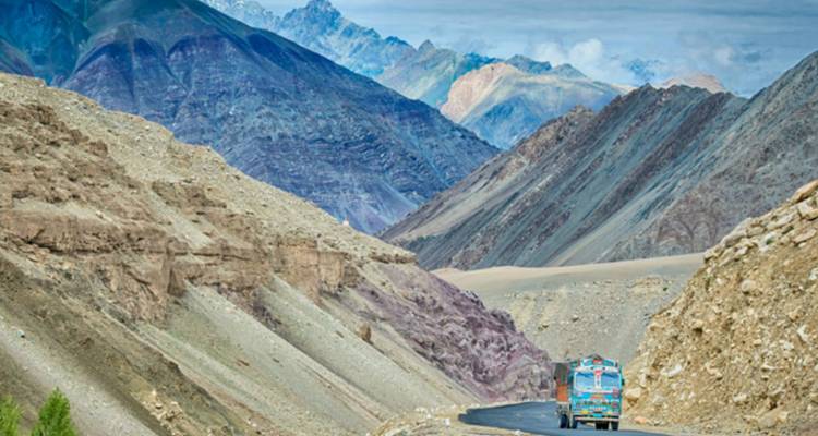 Una serpenteante carretera de montaña se extiende entre escarpadas crestas rocosas mientras un camión de colores brillantes conduce hacia un dramático valle del Himalaya.