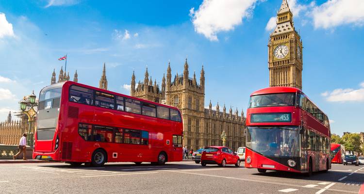 Autobuses clásicos rojos de dos pisos pasando por el Palacio de Westminster y el Big Ben bajo un cielo brillante de Londres.