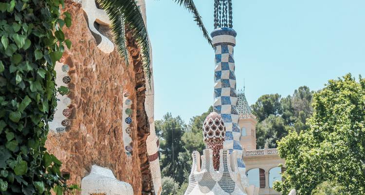 Close-up of mosaic-covered columns and towers inside Park Güell surrounded by greenery.