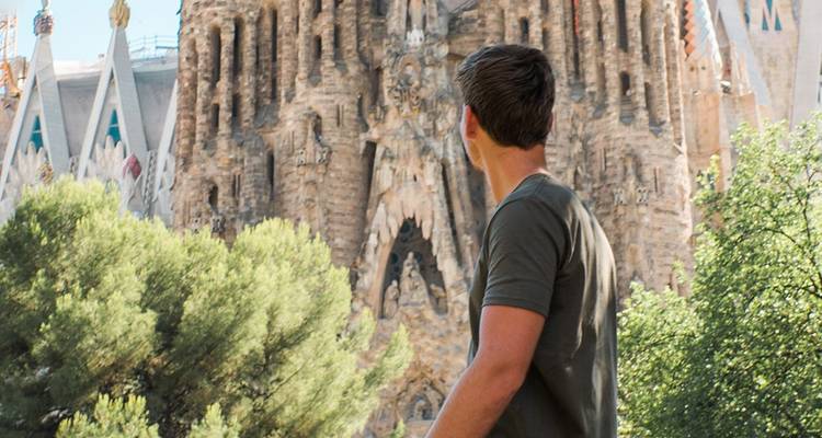 Young man gazes up at the ornate facade of Barcelona’s Sagrada Familia surrounded by green trees