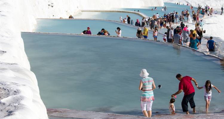 Des foules pataugeant dans les bassins en terrasses turquoise des formations de travertin de Pamukkale ; texte de filigrane visible.