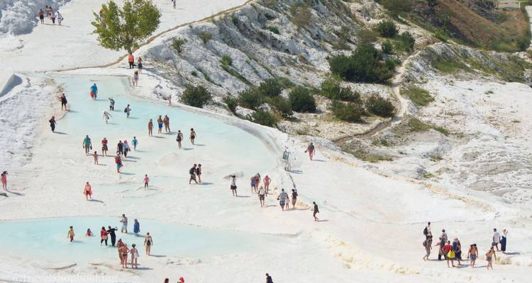 Vue aérienne des terrasses de calcaire blanc et des bassins bleu pâle à Pamukkale avec de nombreux visiteurs ; filigrane présent.