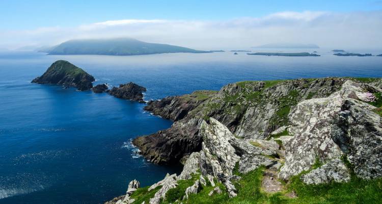 Dramatische Atlantikküste mit zerklüfteten Klippen, die zu tiefblauem Wasser unter einem hellen Himmel in Irland abfallen.