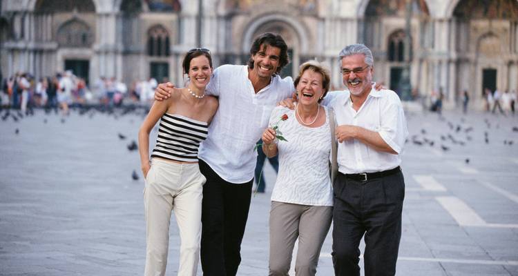 Smiling multigenerational family walking arm-in-arm across St. Mark’s Square in Venice.