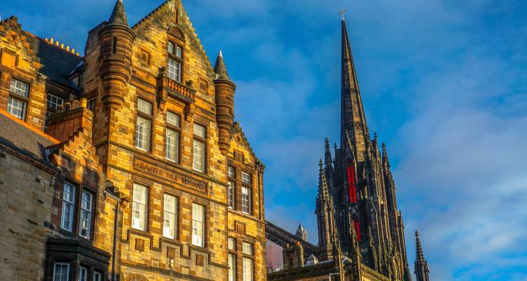 Gothic church spire and ornate stone building glowing in warm sunlight against blue sky