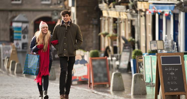 Smiling couple carrying shopping bags strolling along a wet cobblestone street