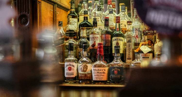 Verschillende whiskyflessen achter de bar uitgestald in warm licht.