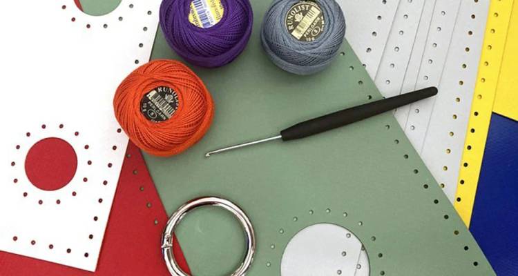 Variados suministros artesanales incluyendo hilo, gancho de crochet y tarjetas perforadas sobre una mesa