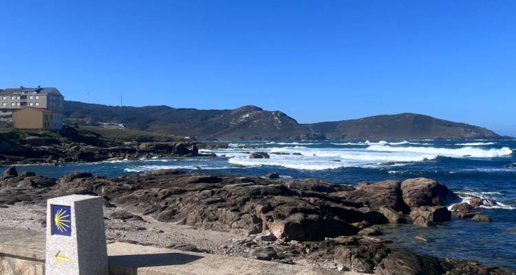 Costa atlántica rocosa con olas chocando y una señal del Camino de Santiago en primer plano.