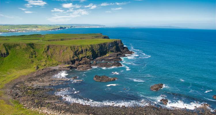 Aerial panorama of rugged basalt shoreline and emerald headland along Northern Ireland's coast.