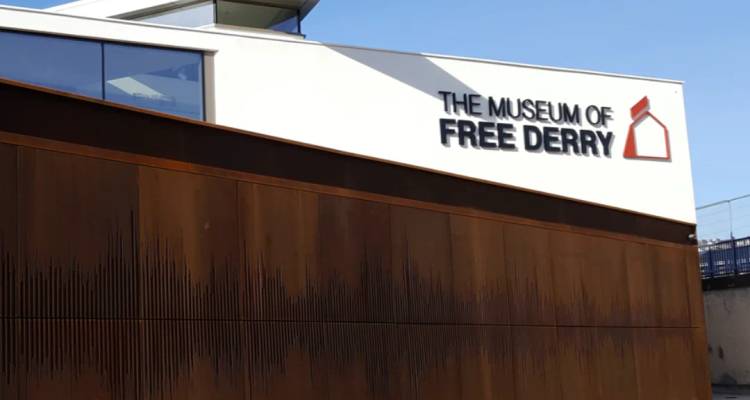 Moderno edificio blanco del museo mostrando el letrero 'The Museum of Free Derry' bajo un cielo azul.