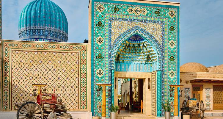 Portail et dôme ornés de carreaux turquoise d'un complexe de mosquée ouzbèke avec des charrettes traditionnelles à l'extérieur.